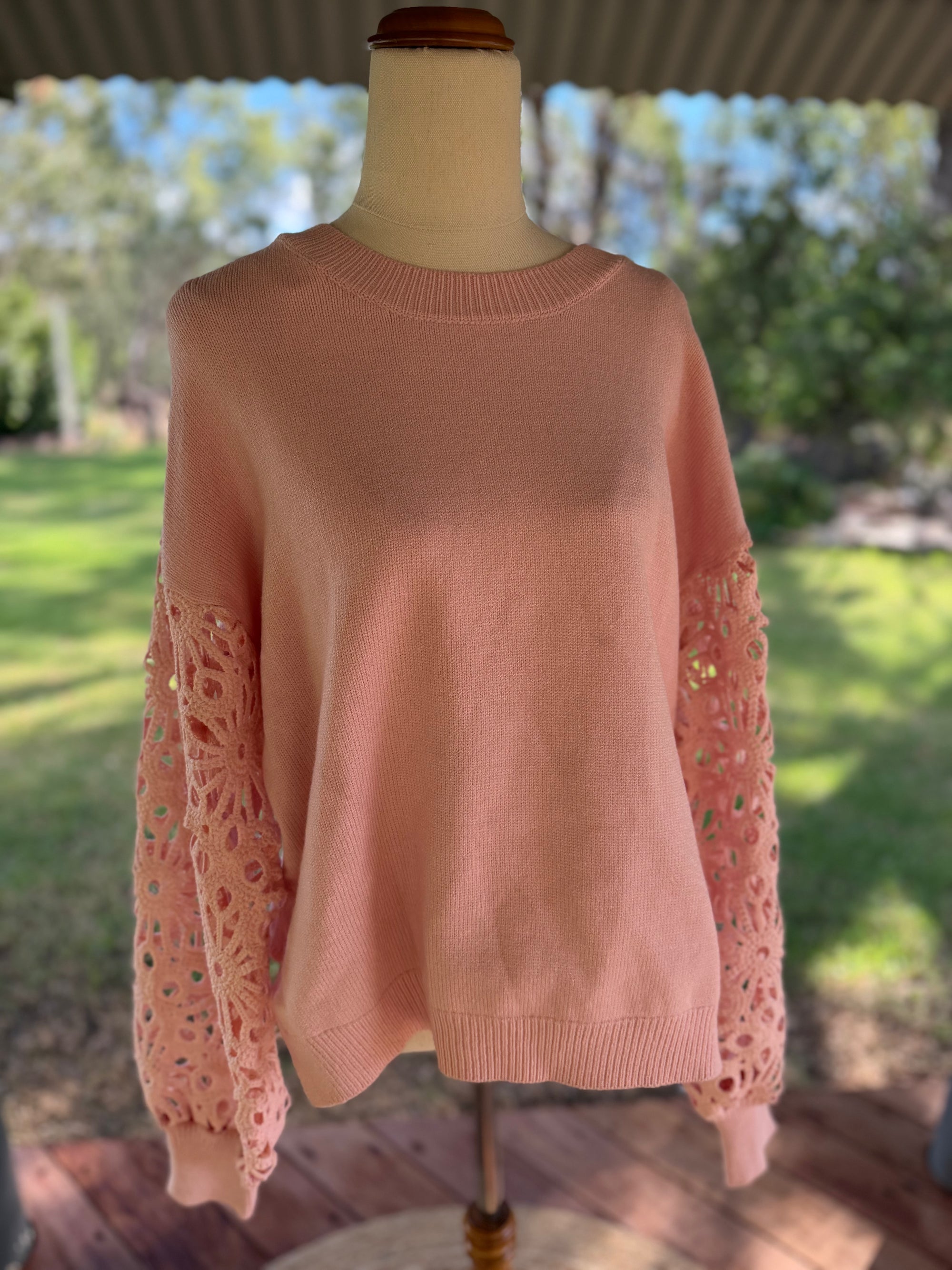 Pink sweater with lace sleeves on a mannequin outdoors.