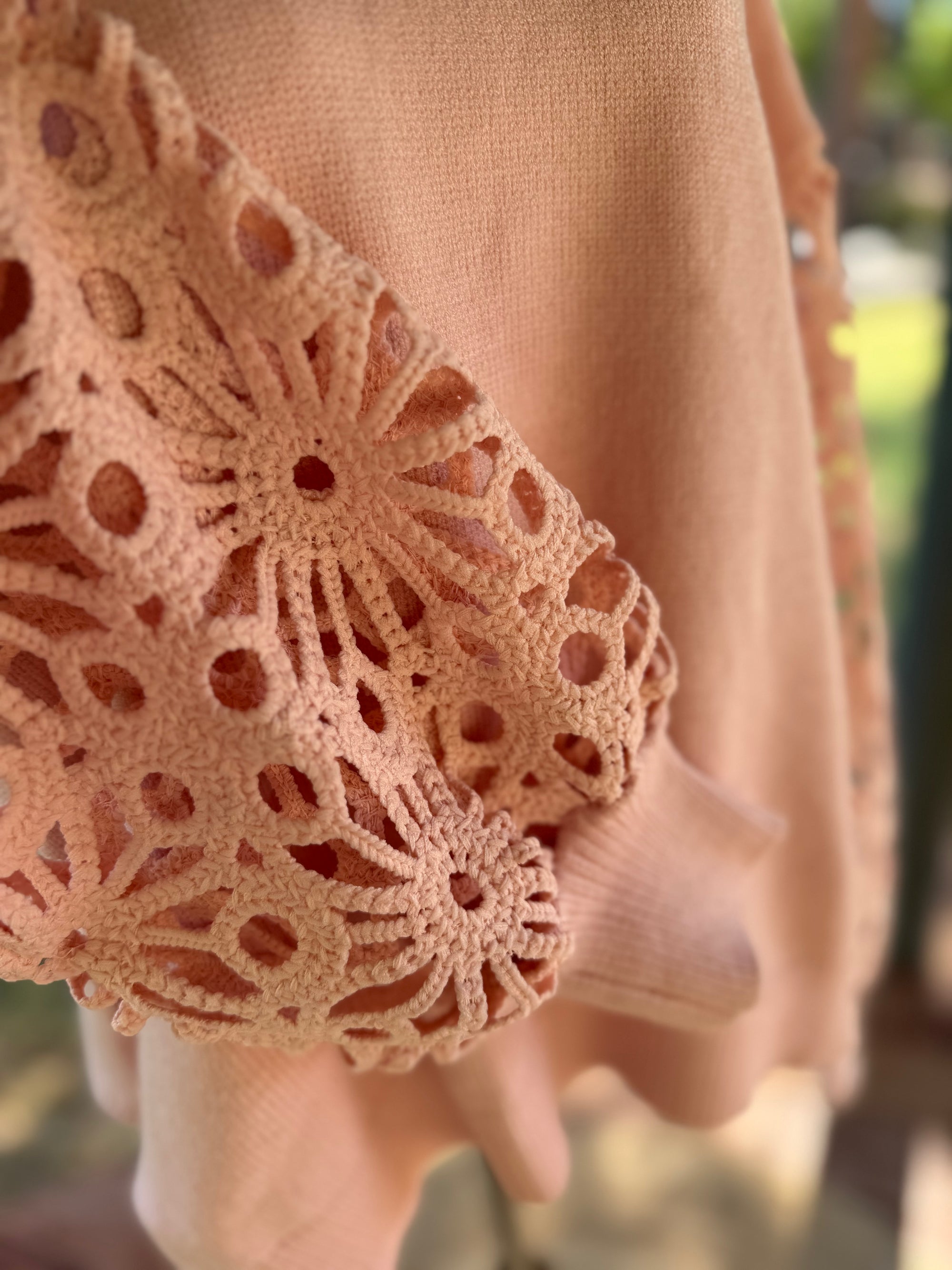 Close-up of a apricot sweater with intricate lace detailing on the sleeve.